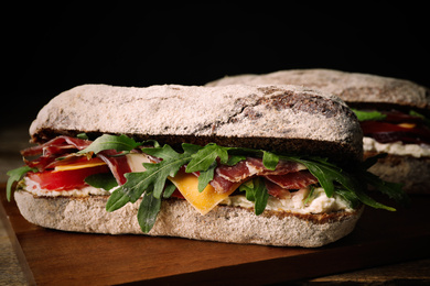 Image of Delicious sandwich with fresh vegetables and prosciutto on wooden table, closeup. Food photography  