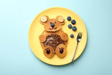 Photo of Creative serving for kids. Plate with cute bear made of pancakes, blueberries, bananas and chocolate paste on light blue table, top view
