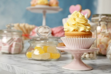 Photo of Stand with cupcake and other sweets on white marble table, space for text. Candy bar
