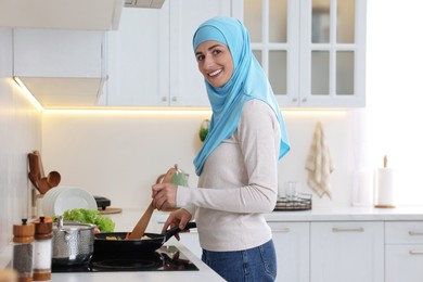 Muslim woman cooking dish in frying pan on cooktop indoors