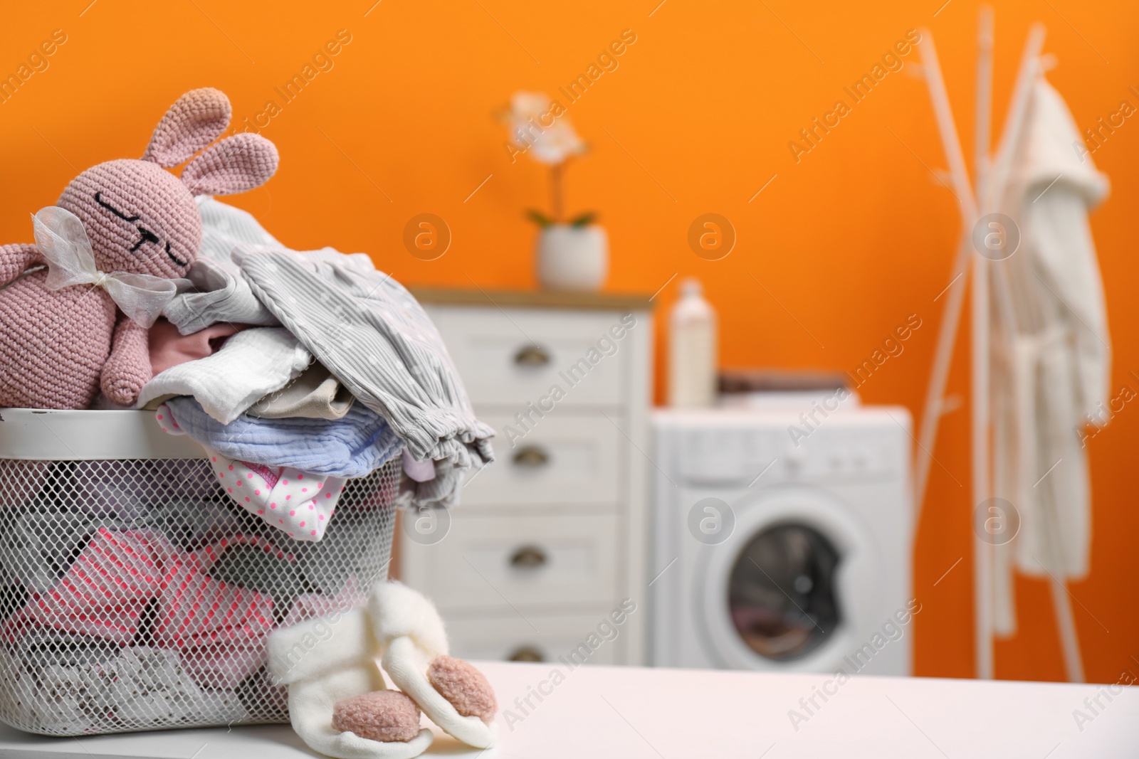 Photo of Laundry basket with baby clothes and toy on table in bathroom, closeup. Space for text