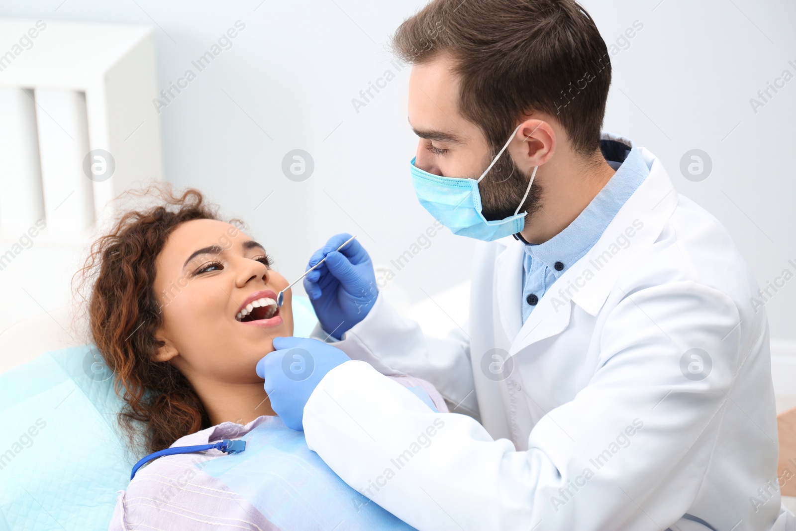 Photo of Dentist examining African-American woman's teeth with mirror in hospital