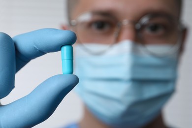 Doctor holding pill on light background, selective focus. Space for text