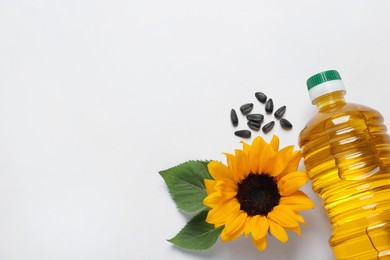 Bottle of cooking oil, sunflowers and seeds on white table, flat lay. Space for text