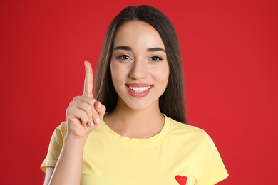 Woman in yellow t-shirt showing number one with her hand on red background