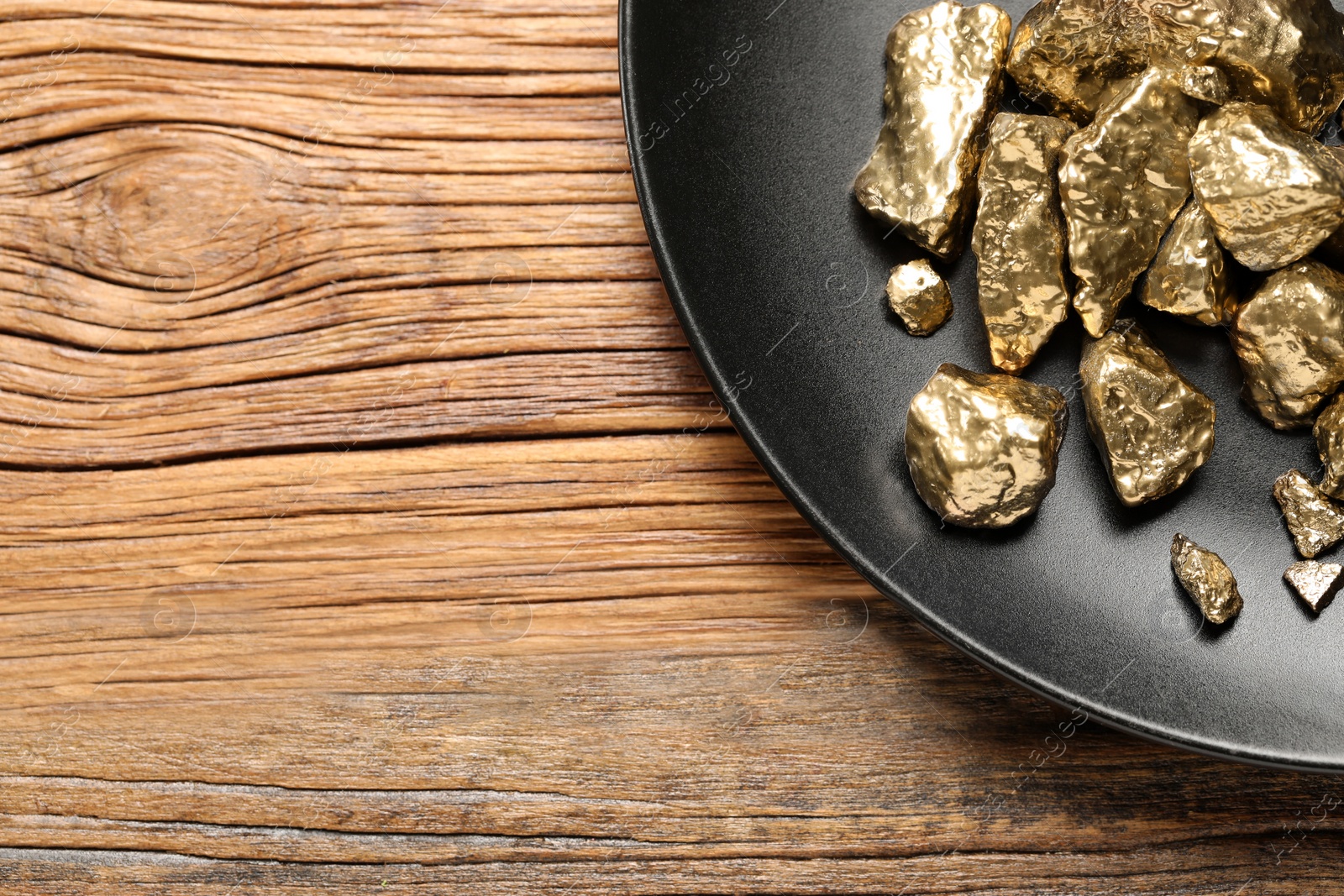 Photo of Plate of gold nuggets on wooden table, top view. Space for text