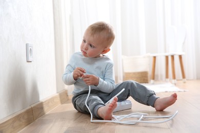 Photo of Little child playing with power strip plug near electrical socket at home. Dangerous situation