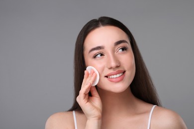 Photo of Beautiful woman removing makeup with cotton pad on gray background