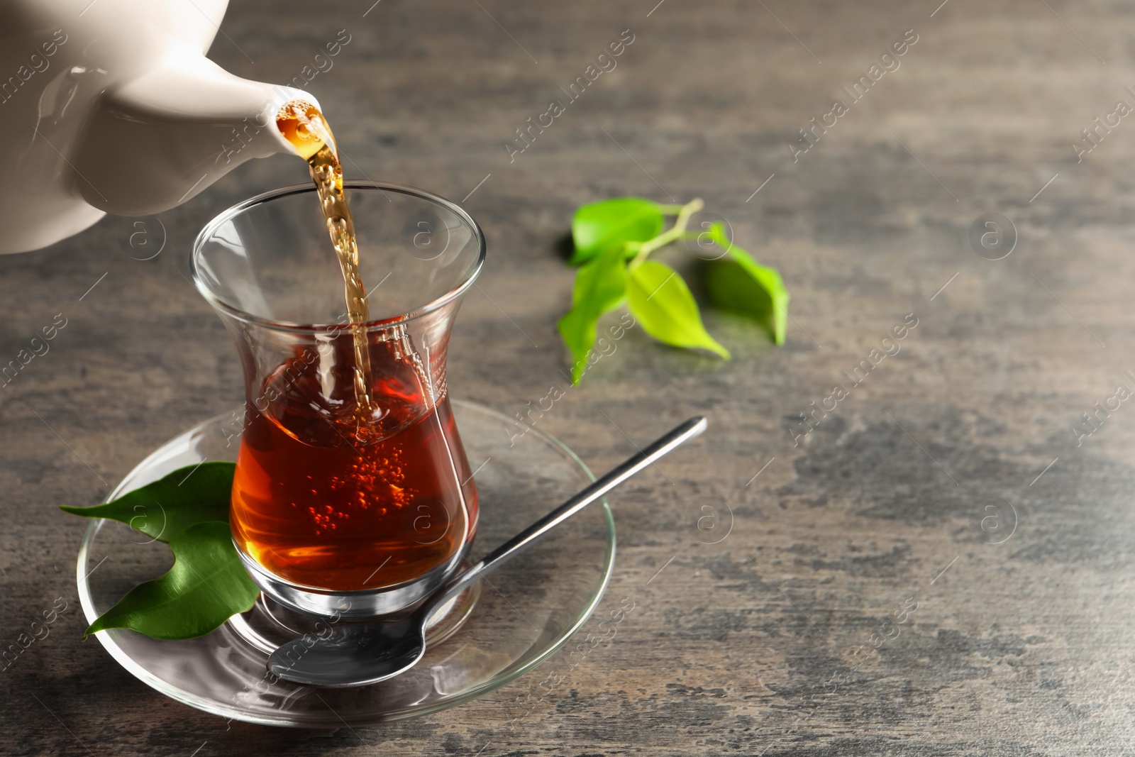 Photo of Pouring traditional Turkish tea from pot into glass on grey table, space for text