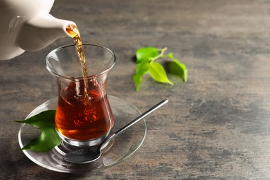 Pouring traditional Turkish tea from pot into glass on grey table, space for text