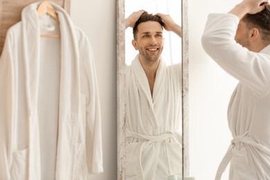 Photo of Young man looking at himself in mirror indoors