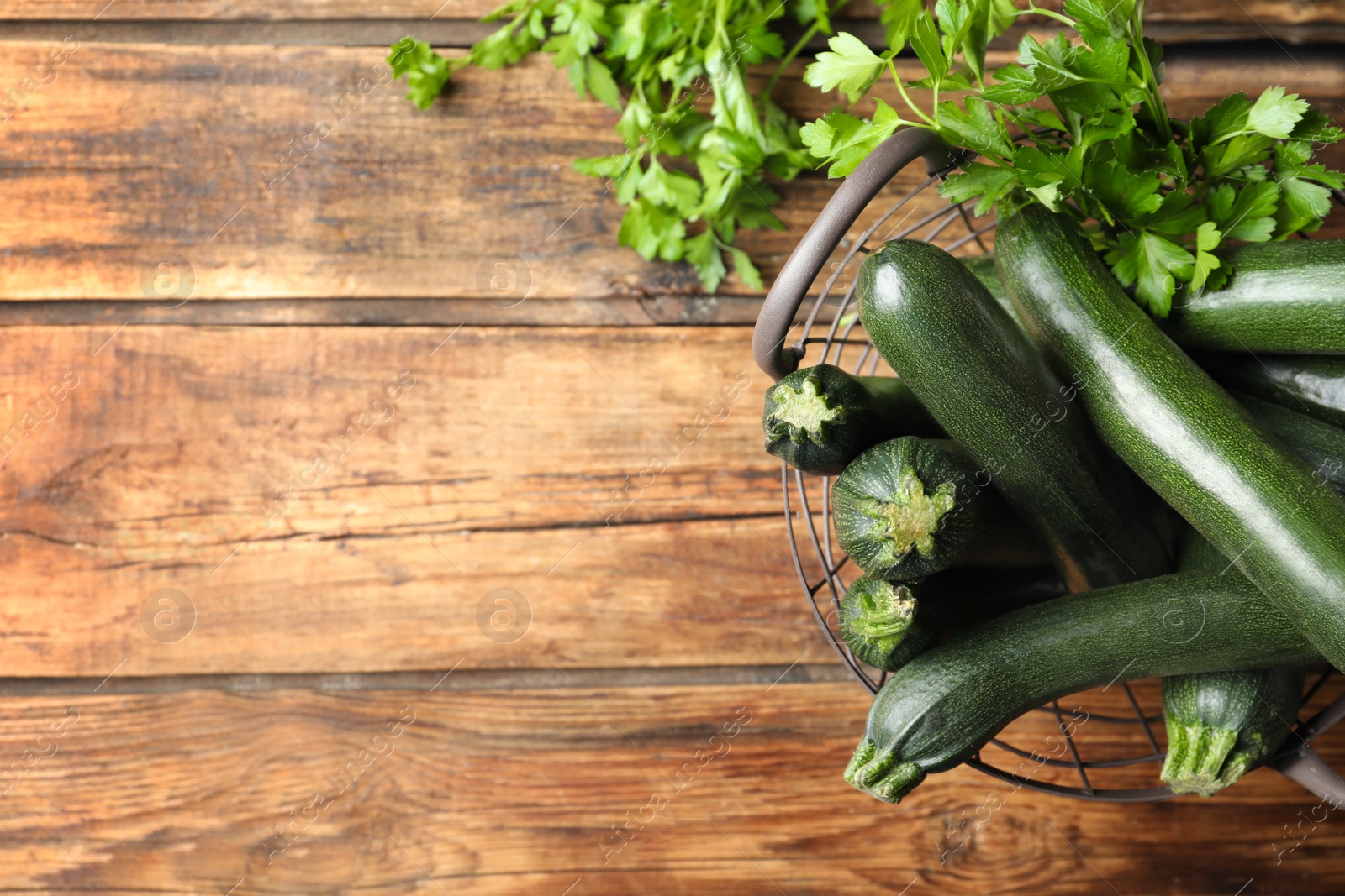 Photo of Basket with green zucchinis on wooden table, flat lay. Space for text