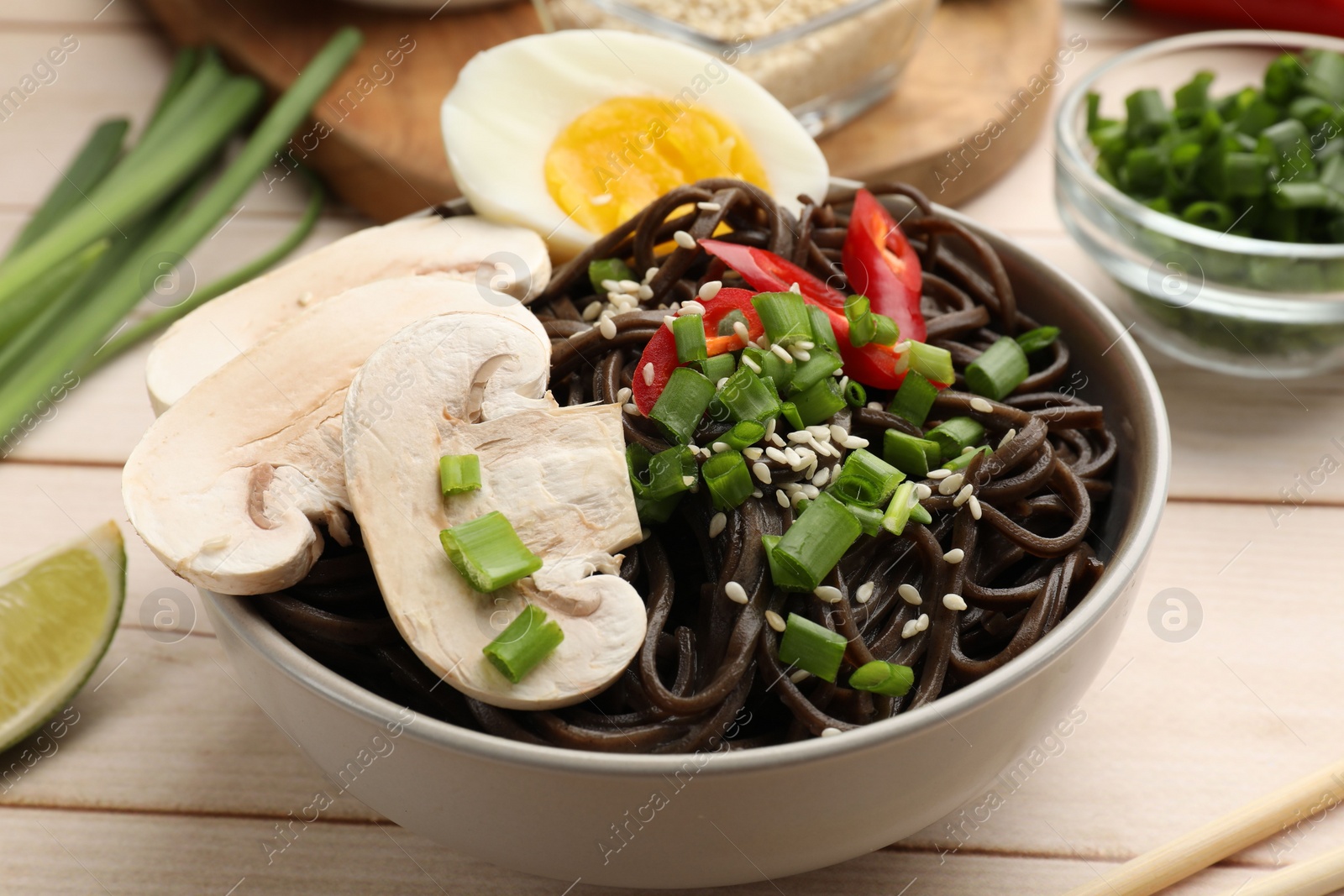 Photo of Tasty buckwheat noodles (soba) with mushrooms, onion, egg and chili pepper in bowl on wooden table, closeup