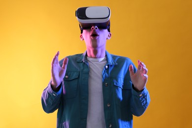 Young man with virtual reality headset on yellow background. Space for text