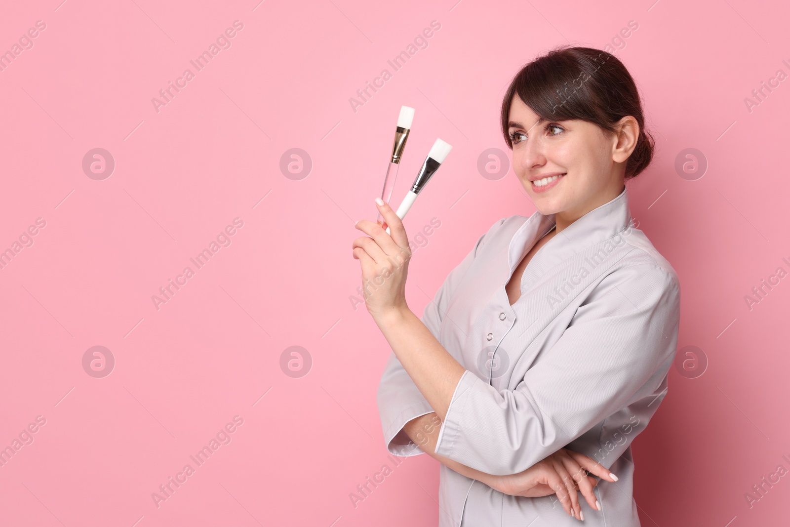 Photo of Cosmetologist with cosmetic brushes on pink background, space for text