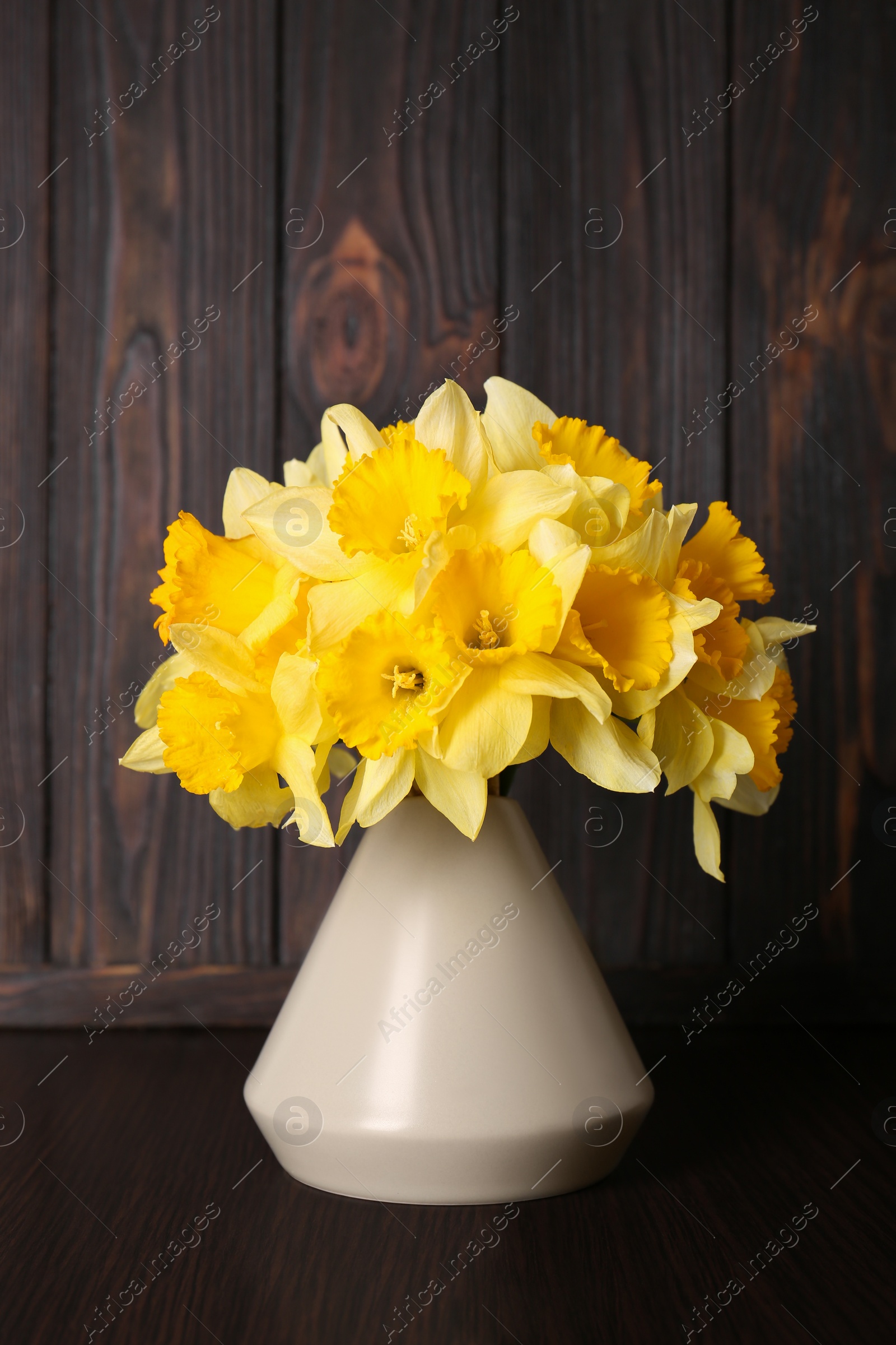 Photo of Bouquet of beautiful yellow daffodils in vase on wooden table