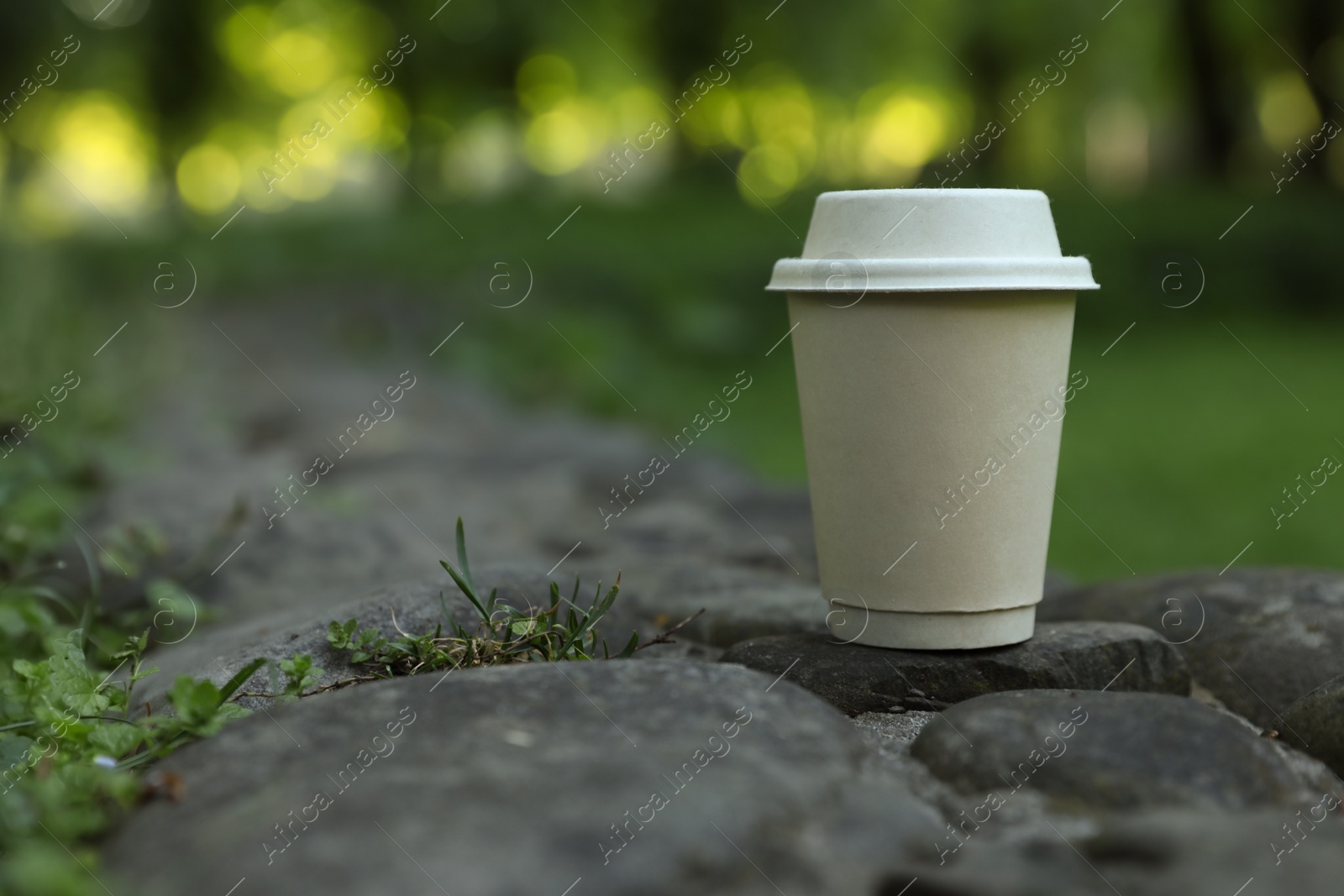 Photo of Cardboard takeaway coffee cup with lid on stones outdoors, space for text