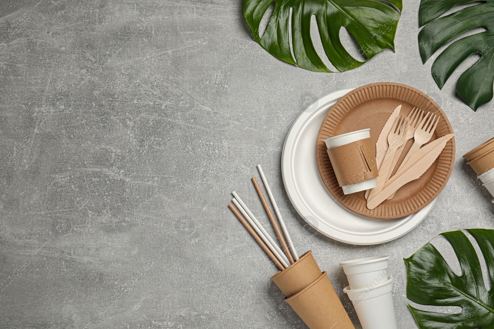 Photo of Flat lay composition with disposable tableware and monstera leaves on light grey background, space for text