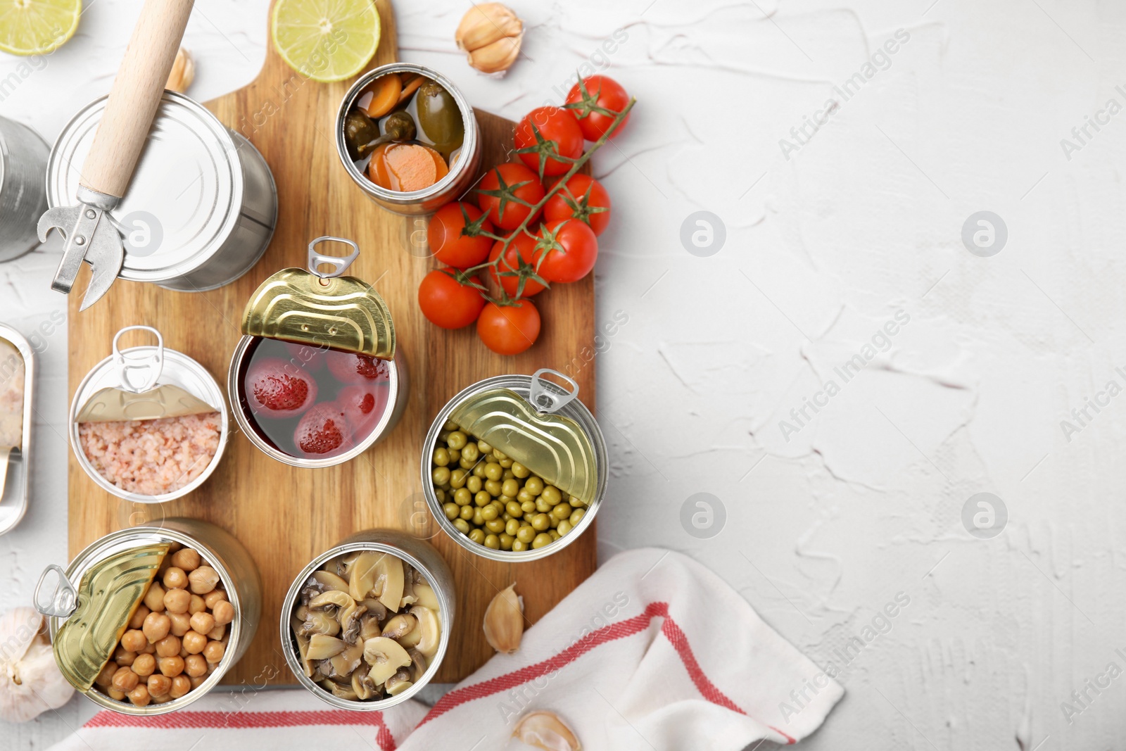 Photo of Open tin cans with different preserved products on white textured table, flat lay. Space for text