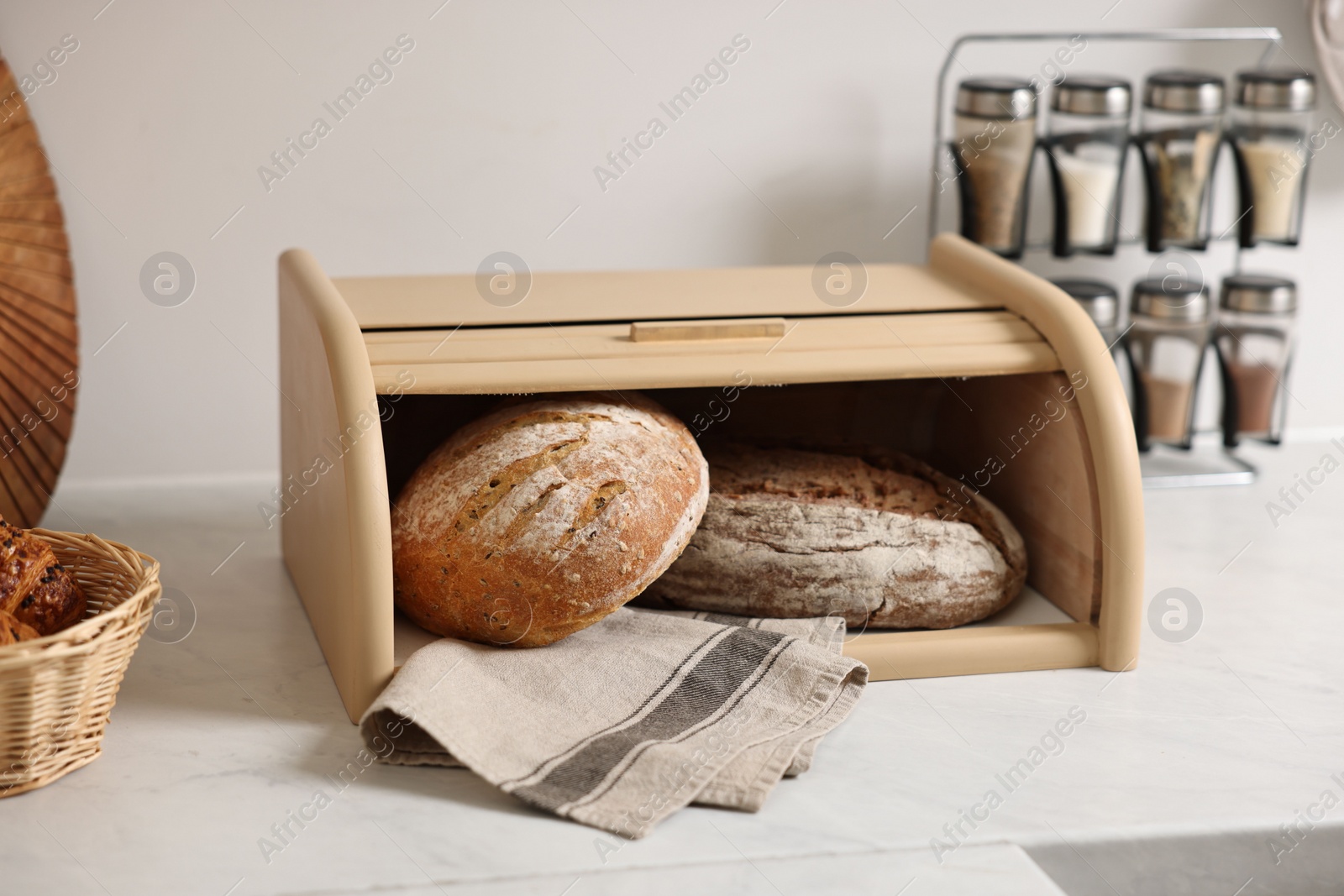 Photo of Wooden bread basket with freshly baked loaves on white marble table in kitchen