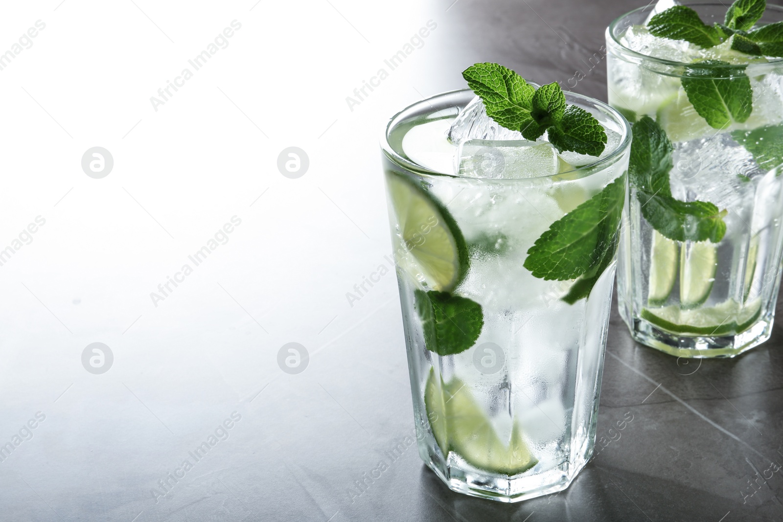 Photo of Tasty Mojito cocktail with ice cubes on light grey table, closeup. Space for text