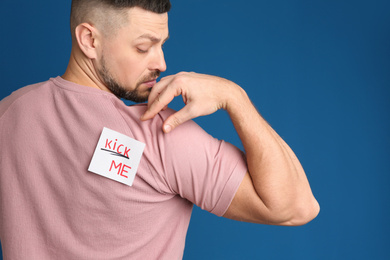 Photo of Man with KICK ME sticker on back against blue background. April fool's day