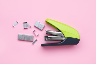 Photo of New bright stapler with staples on pink background, fat lay. School stationery