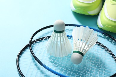 Photo of Feather badminton shuttlecocks, rackets and sneakers on light blue background