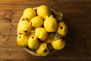 Photo of Tasty ripe quince fruits with water drops in bowl on wooden table, top view