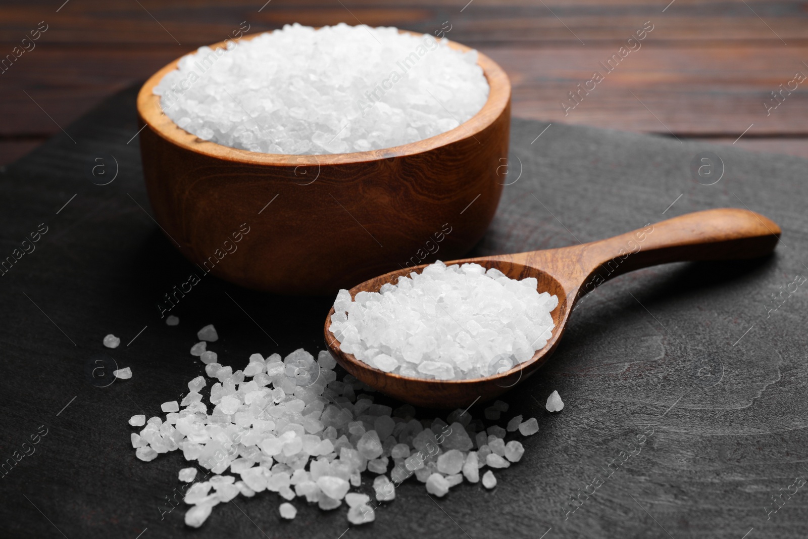 Photo of Spoon and bowl of natural sea salt on wooden table