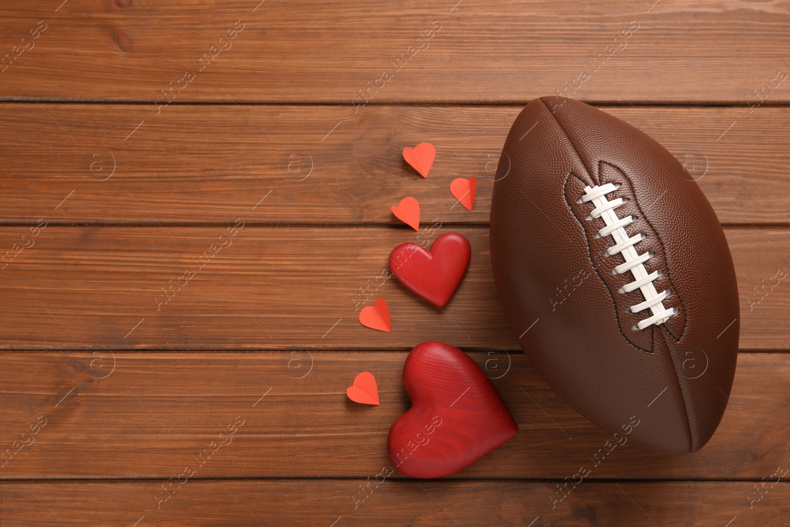 Photo of American football ball and hearts on wooden background, flat lay. Space for text