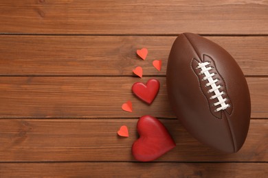 Photo of American football ball and hearts on wooden background, flat lay. Space for text