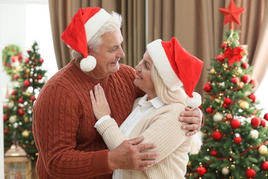 Happy mature couple in Santa hats at home. Christmas celebration