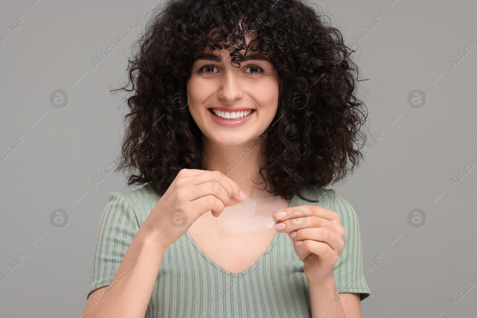 Photo of Young woman holding teeth whitening strips on grey background