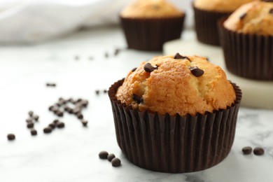 Photo of Delicious sweet muffin with chocolate chips on white marble table, closeup. Space for text