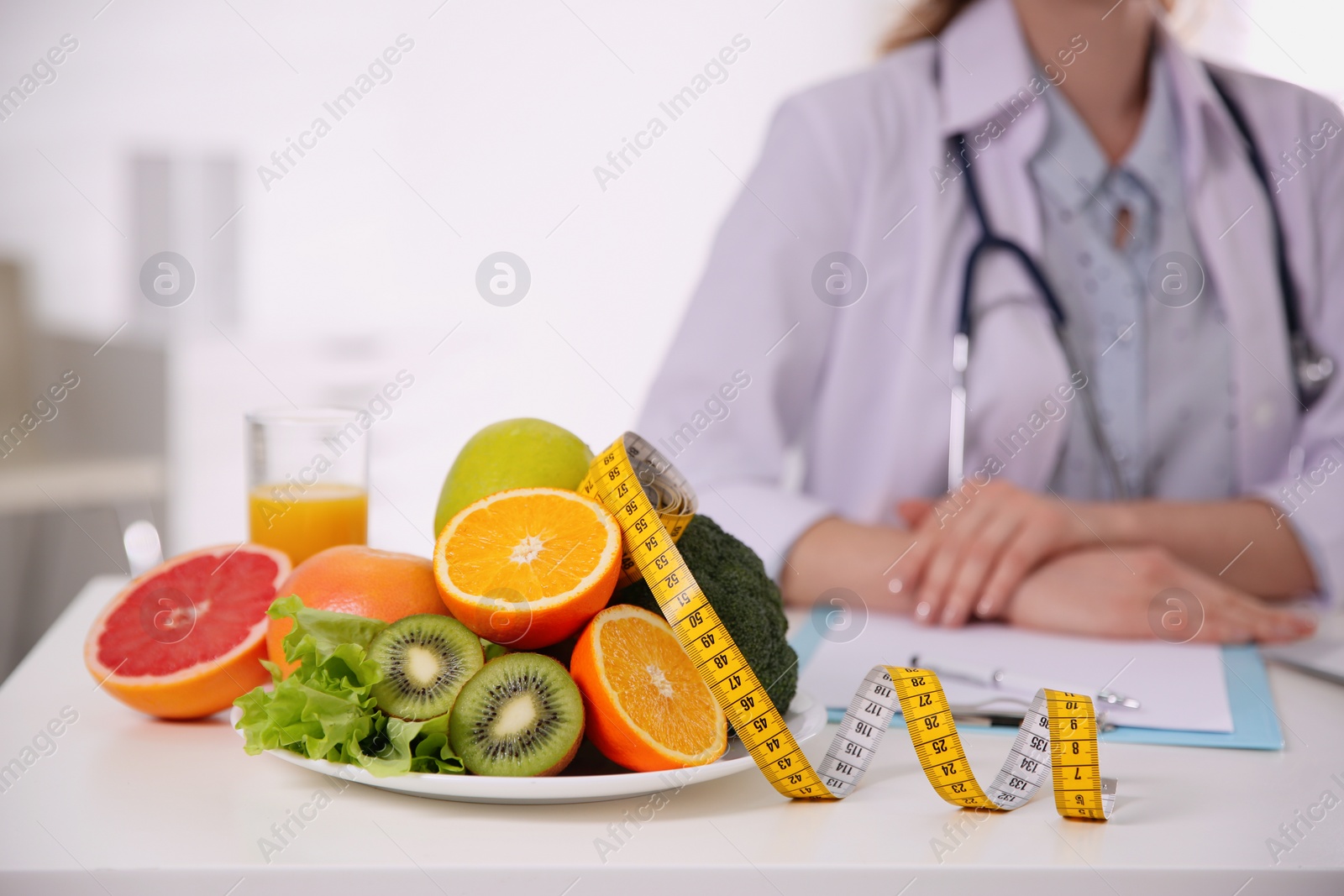 Photo of Nutritionist at desk with fruits, vegetables and measuring tape in office, closeup