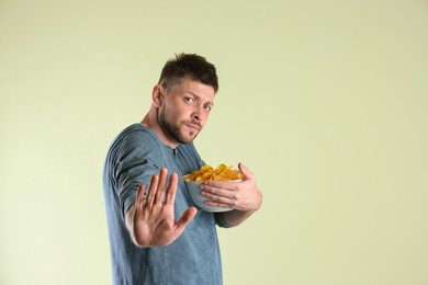 Photo of Greedy man hiding bowl with chips on light background, space for text