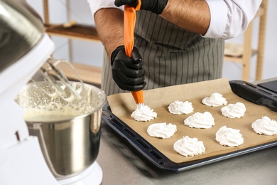 Photo of Pastry chef preparing meringues at table in kitchen, closeup
