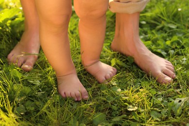 Photo of Woman with her child walking barefoot on green grass outdoors, closeup
