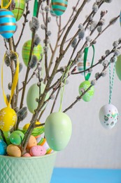 Photo of Beautiful willow branches with painted eggs in pot on light background, closeup. Easter decor