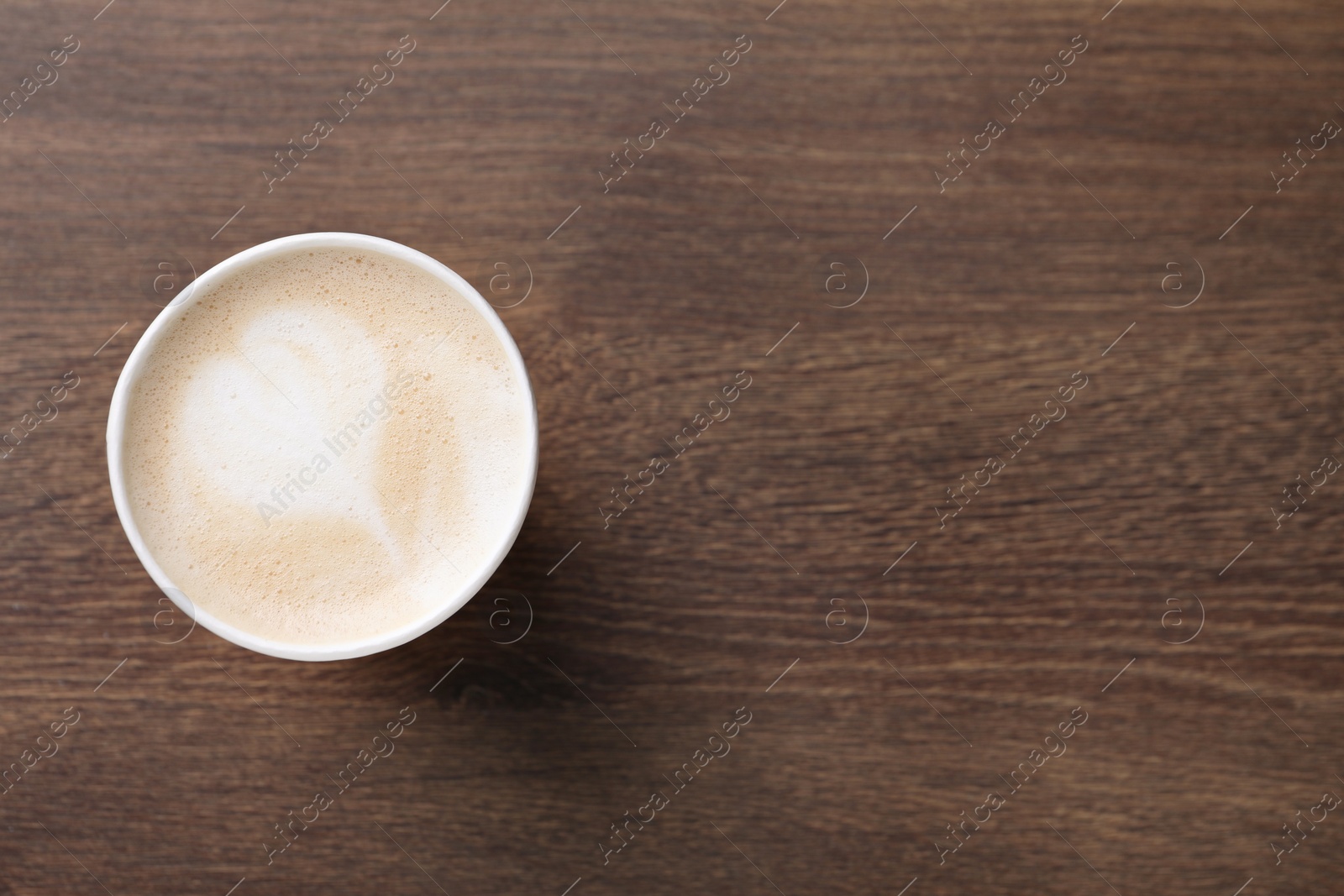 Photo of To-go drink. Tasty coffee in paper cup on wooden table, top view. Space for text