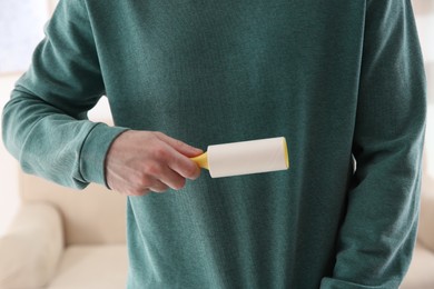 Man cleaning green sweatshirt with lint roller on light background, closeup