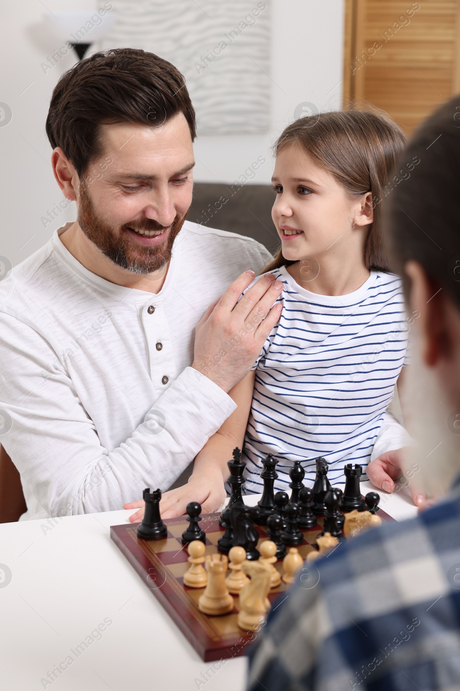 Photo of Family playing chess together at table in room