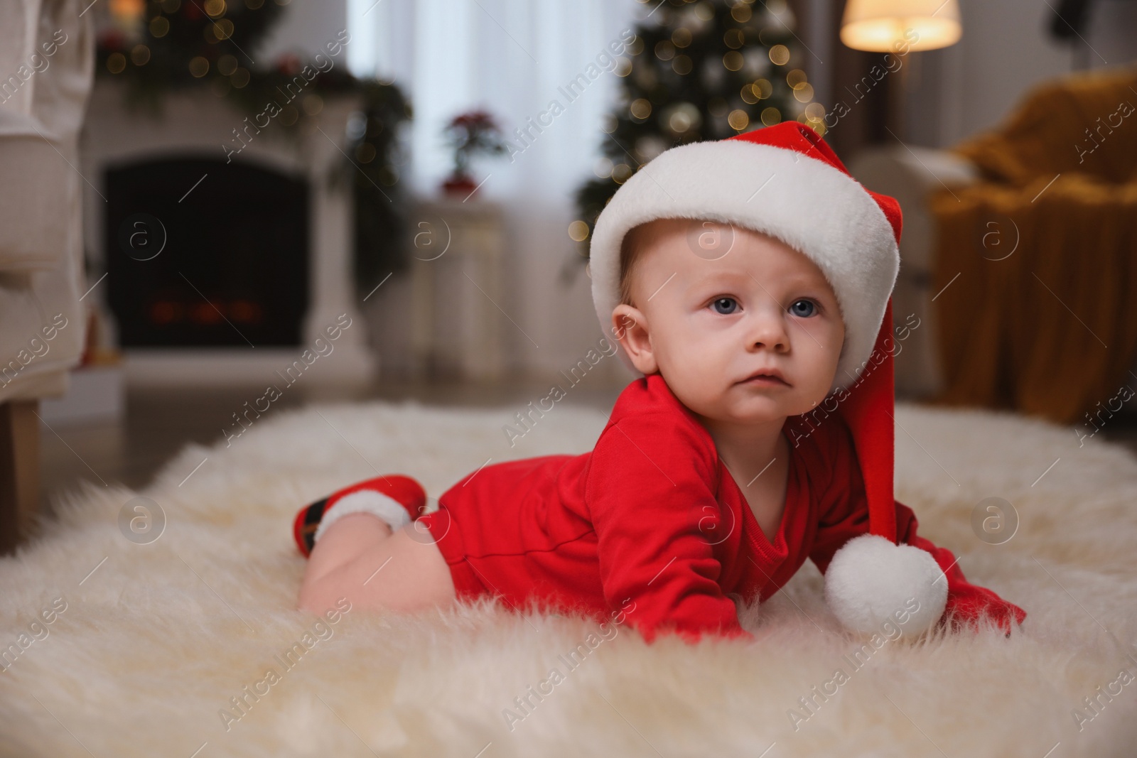 Photo of Cute little baby in red bodysuit and Santa hat on floor at home. Christmas suit