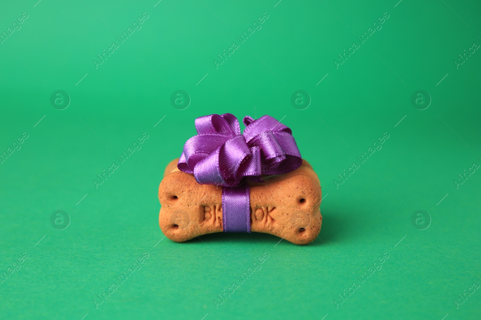 Photo of Bone shaped dog cookie with purple bow on green background