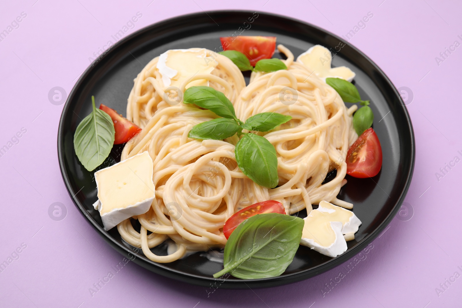 Photo of Delicious pasta with brie cheese, tomatoes and basil leaves on violet table, closeup