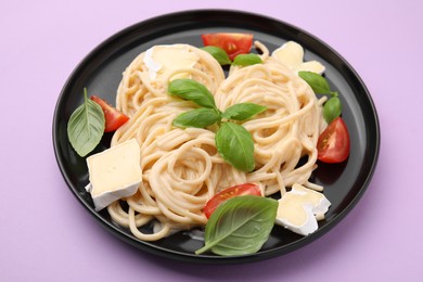 Delicious pasta with brie cheese, tomatoes and basil leaves on violet table, closeup