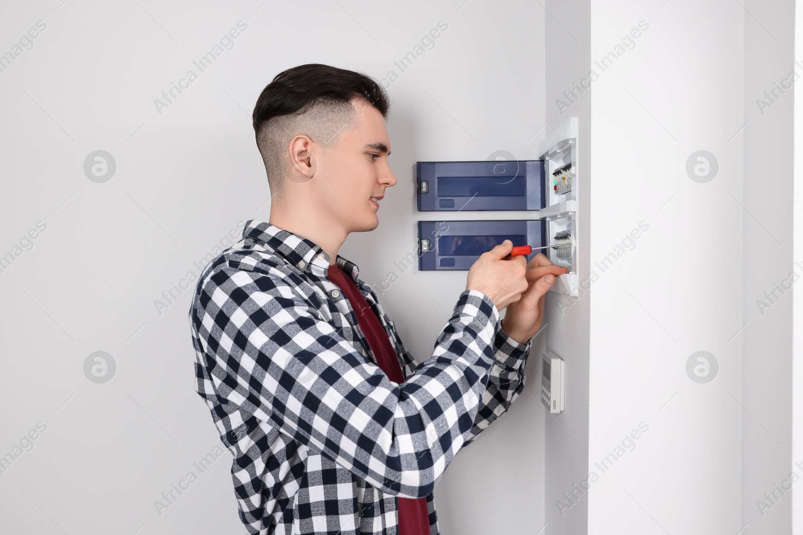 Photo of Young handyman with screwdriver repairing electrical panel board indoors