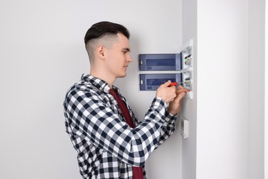 Young handyman with screwdriver repairing electrical panel board indoors