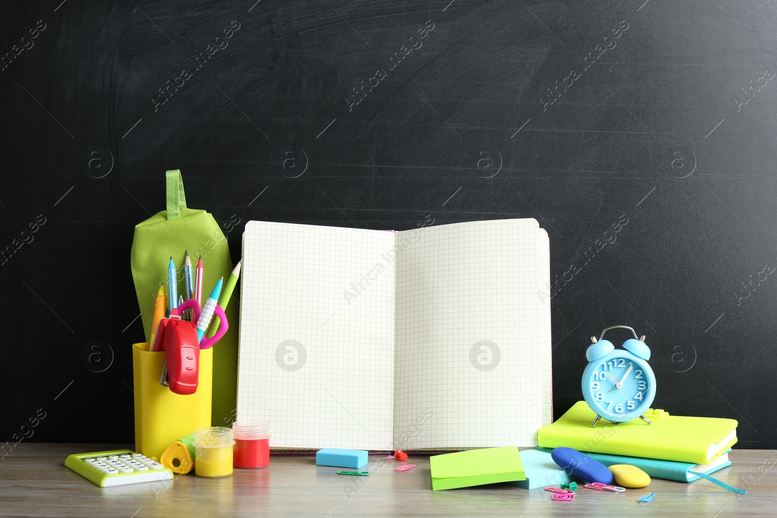 Photo of Different school stationery and blank notebook on table near chalkboard. Space for text